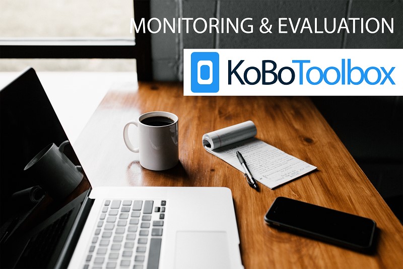 Picture of a desk with a laptop, coffee mug, smartphone, notepad and KoBoToolbox logo at top right